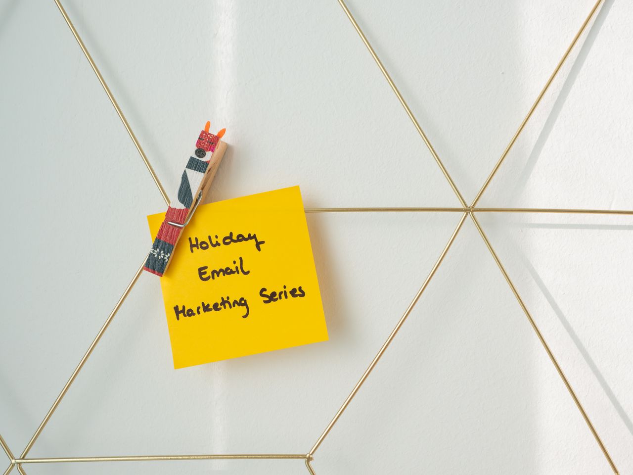 about-01 Post-it jaune vif avec un message de marketing par email pour les fêtes, fixé sur un mur en grille métallique.